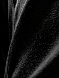 Close-up on textured black denim jeans on a dark matte background.