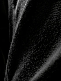 Close-up on textured black denim jeans on a dark matte background.