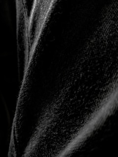 A close-up view of black denim fabric, highlighting the texture and weave of the material with varying shades of black and gray.