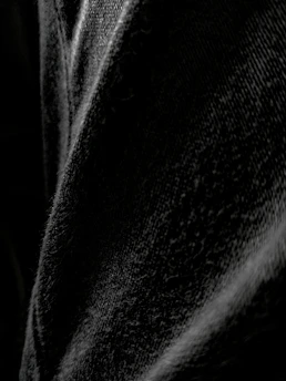 A pair of classic black denim jeans laid out flat with subtle lighting highlighting the texture.