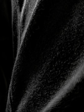 A close-up view of black denim fabric, highlighting the texture and weave of the material with varying shades of black and gray.