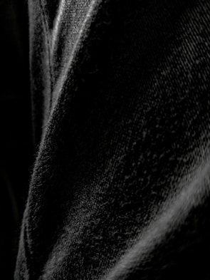 Close-up of TQS Black Jeans details with strong lighting highlighting the fabric texture.