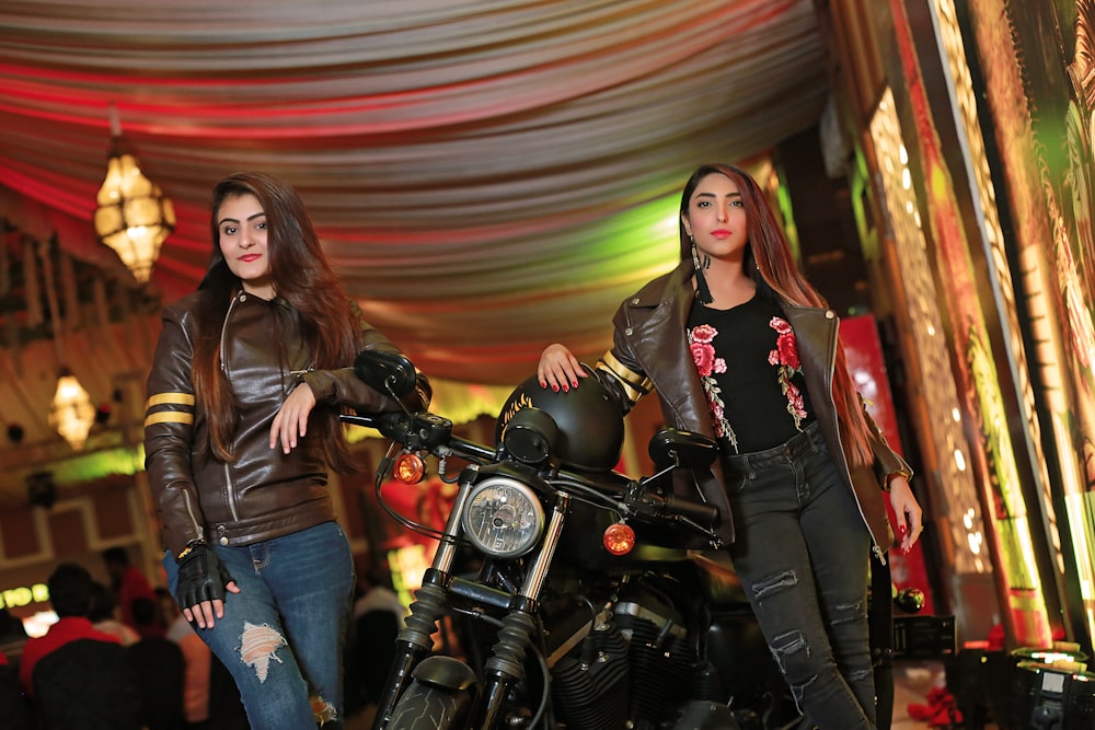 woman in black leather jacket standing beside black motorcycle