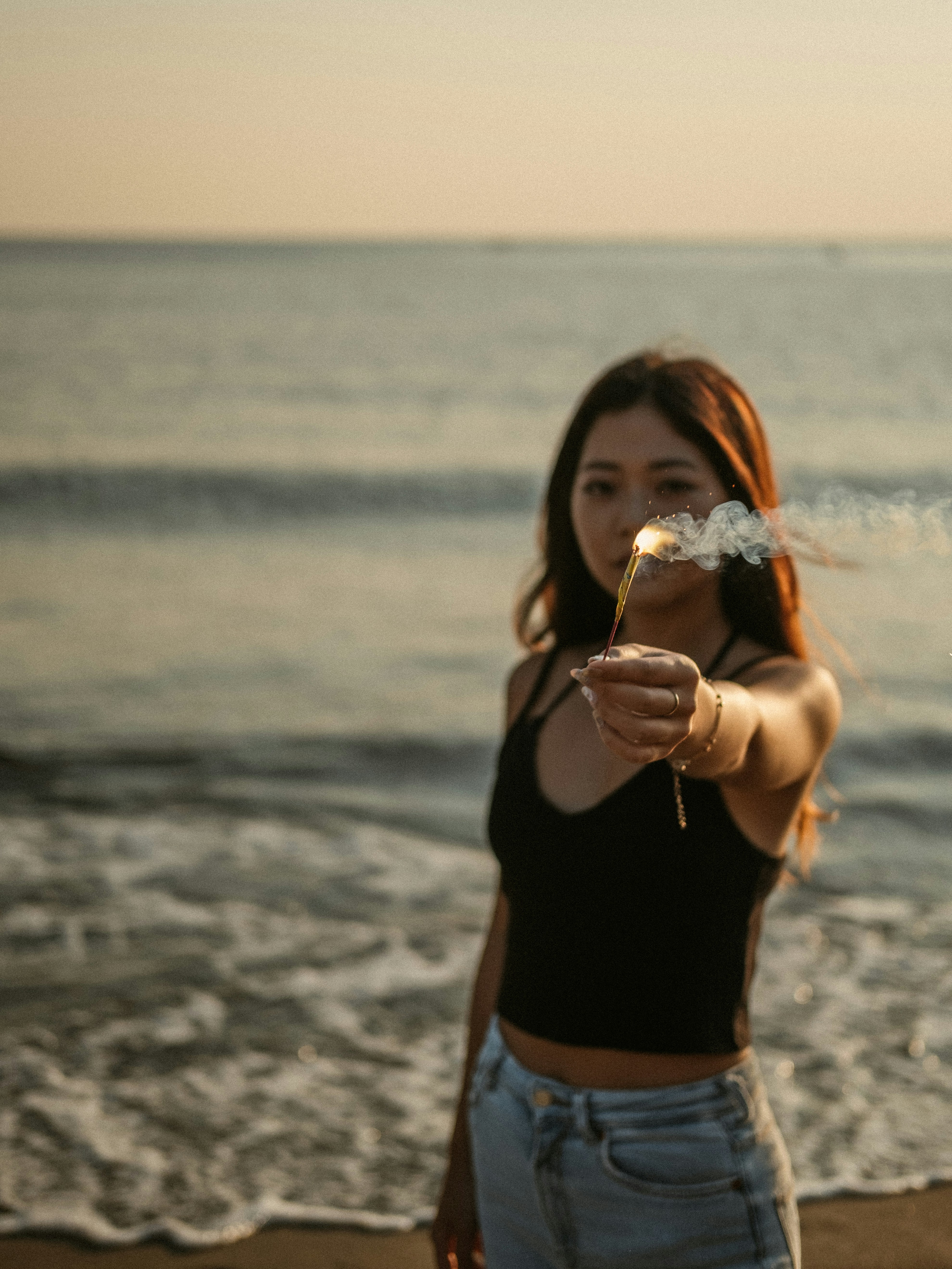 a woman standing on a beach holding a cigarette