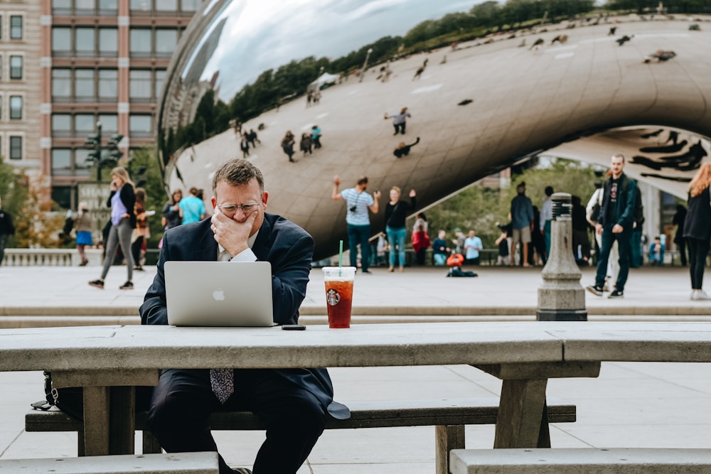 man in black jacket sitting on chair in front of macbook