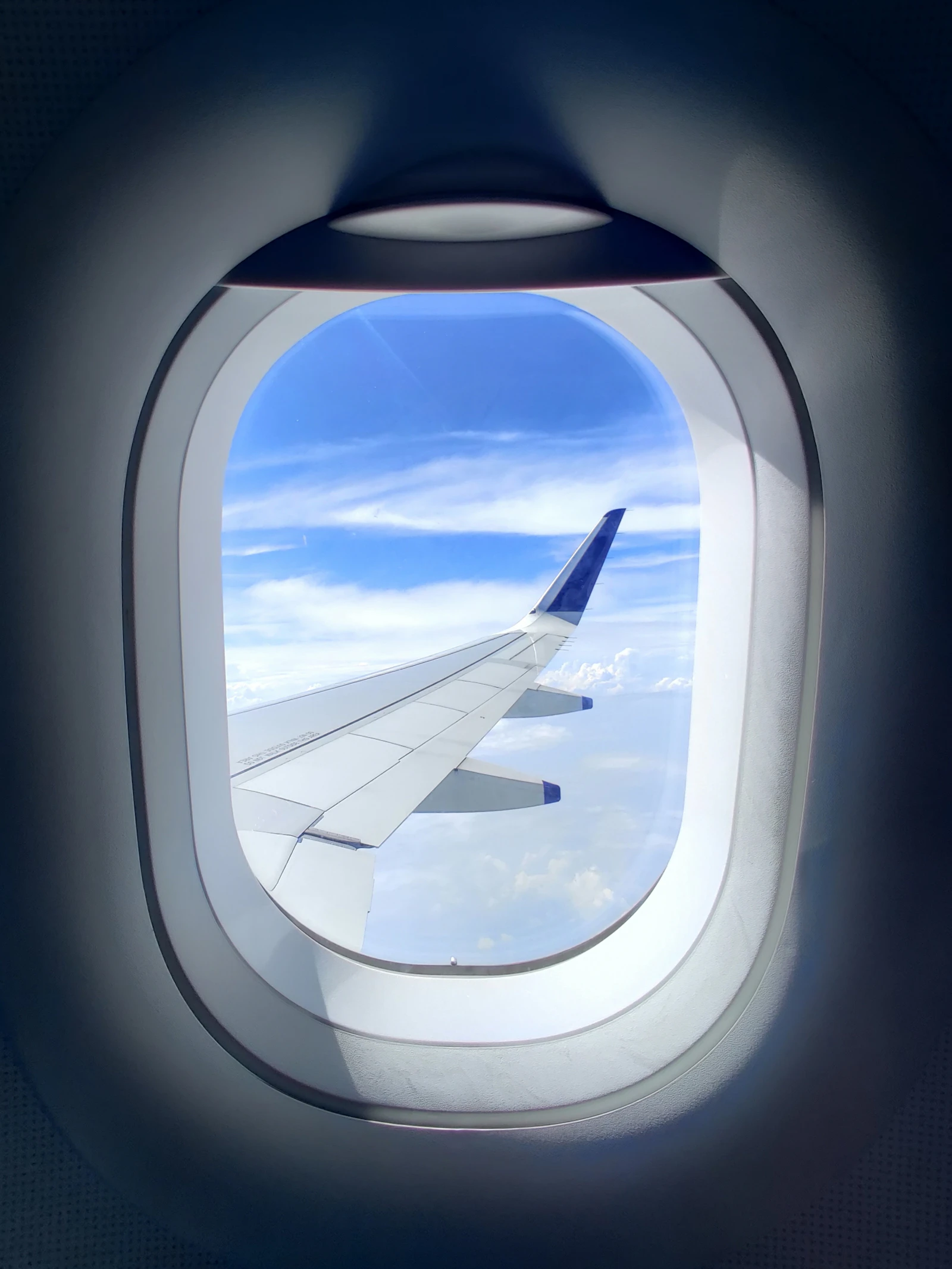 The view from a passenger window seat showing the airliner wing against a bright blue sky with light clouds during a smooth leg of the trip