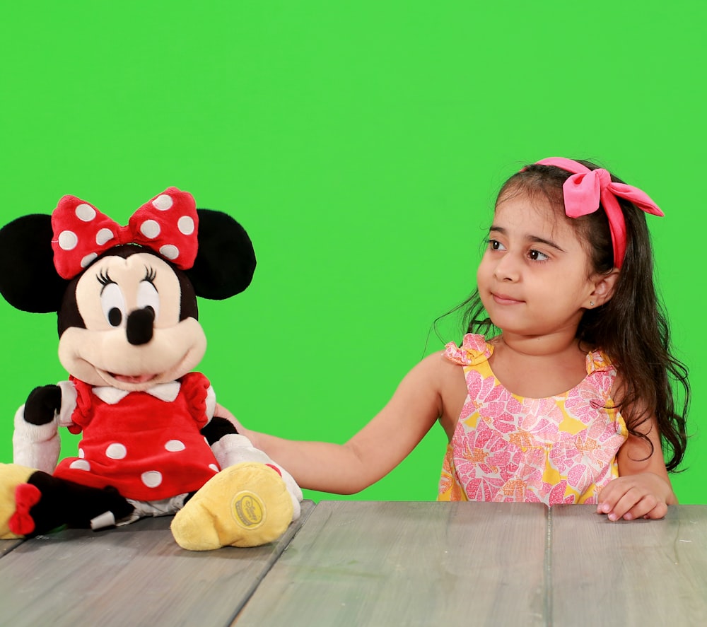 girl in minnie mouse dress sitting beside minnie mouse plush toy