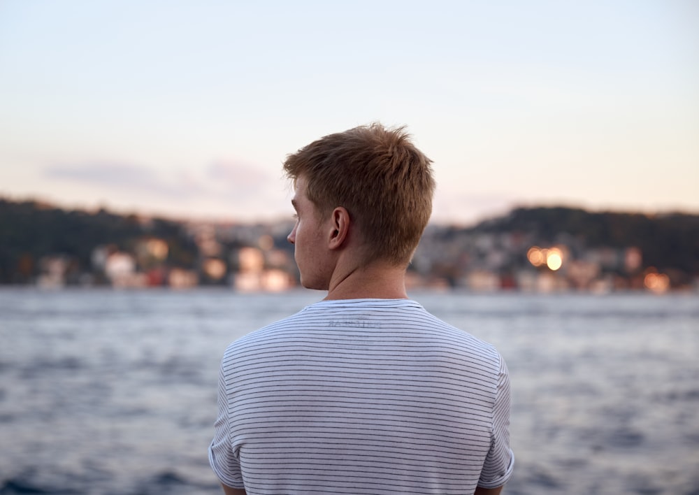 homme en chemise rayée blanche et bleue regardant la mer pendant la journée