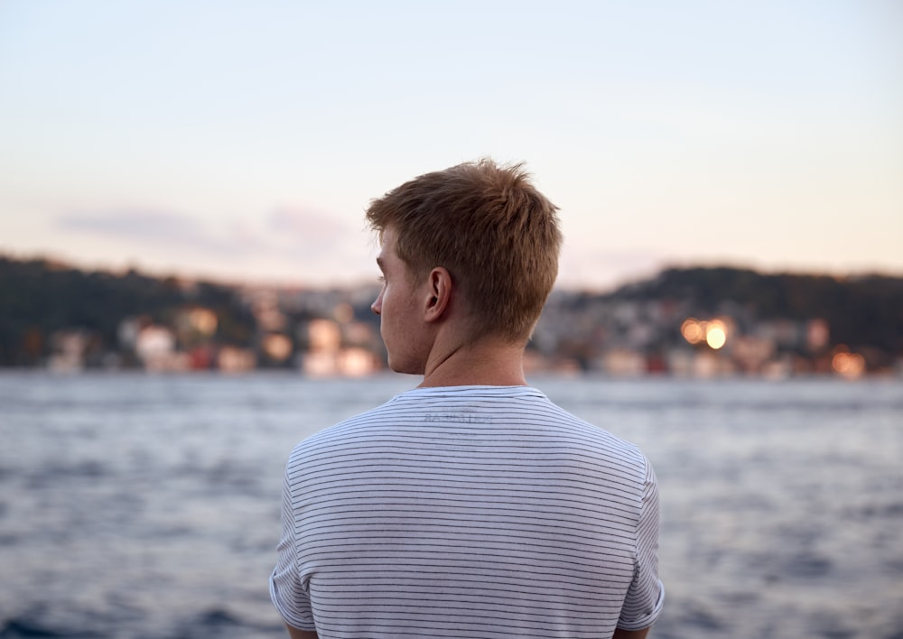 uomo in camicia a righe bianche e blu che guarda il mare durante il giorno
