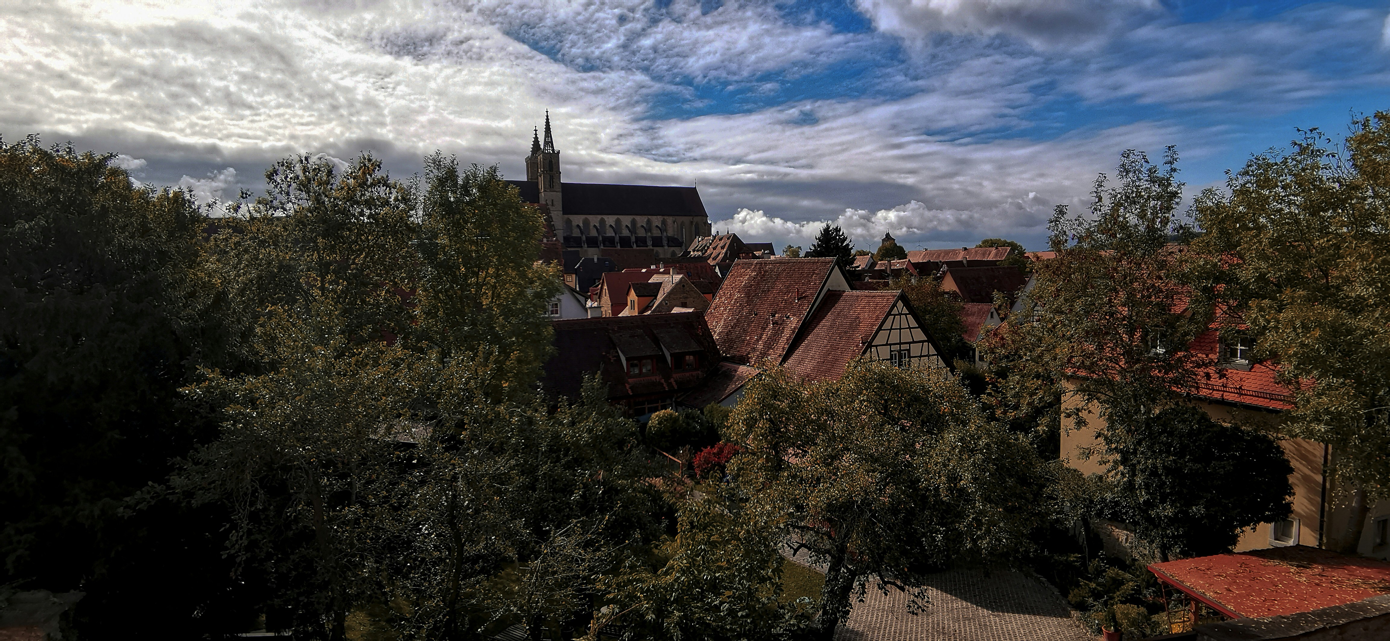 brown and black concrete house surrounded by green trees under white clouds and blue sky during