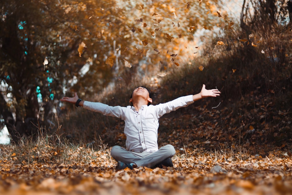 woman in white long sleeve shirt and blue denim jeans sitting on brown dried leaves during