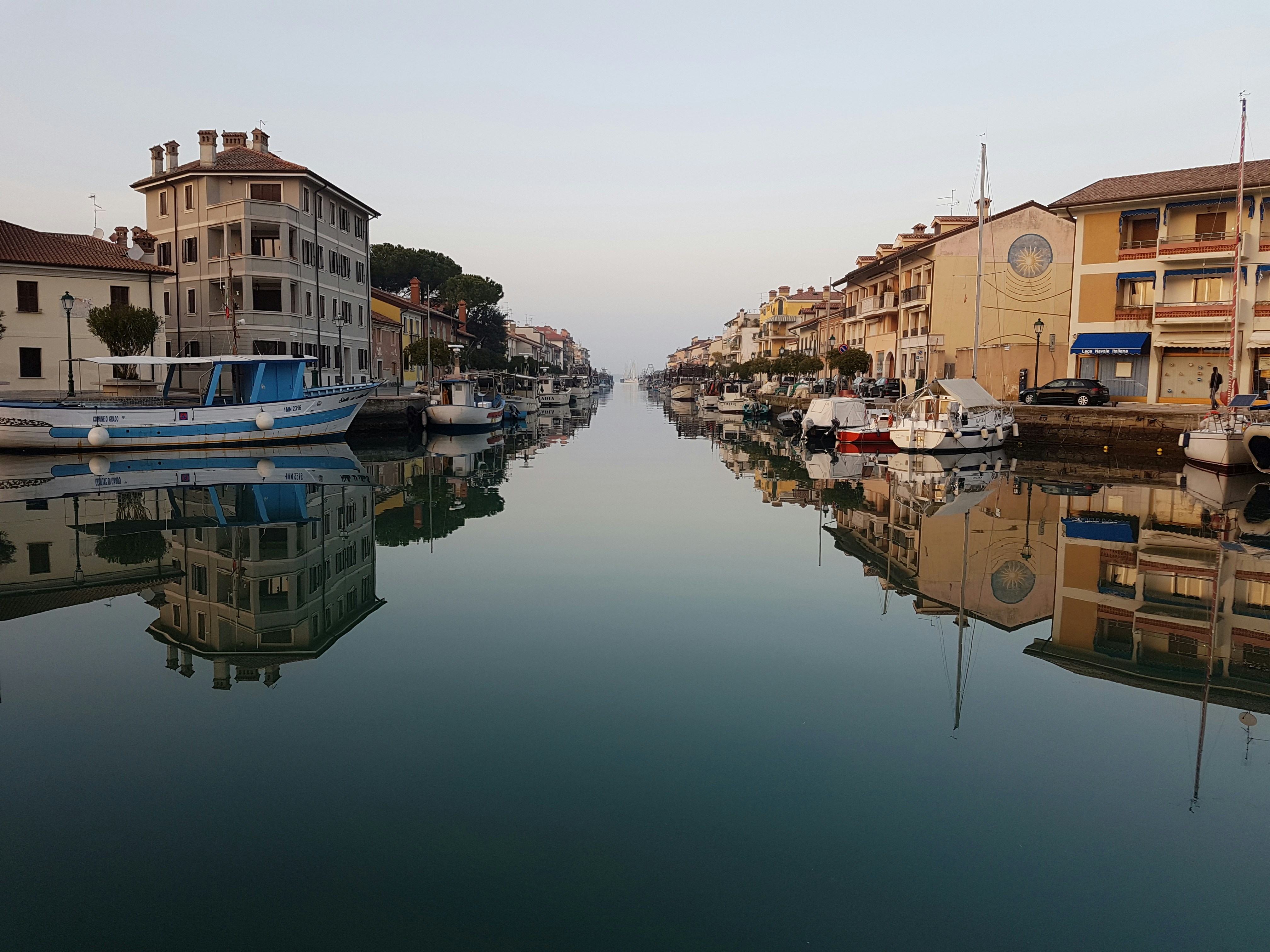 brown concrete building beside river during daytime, reflection of buildings in Grado, Italy