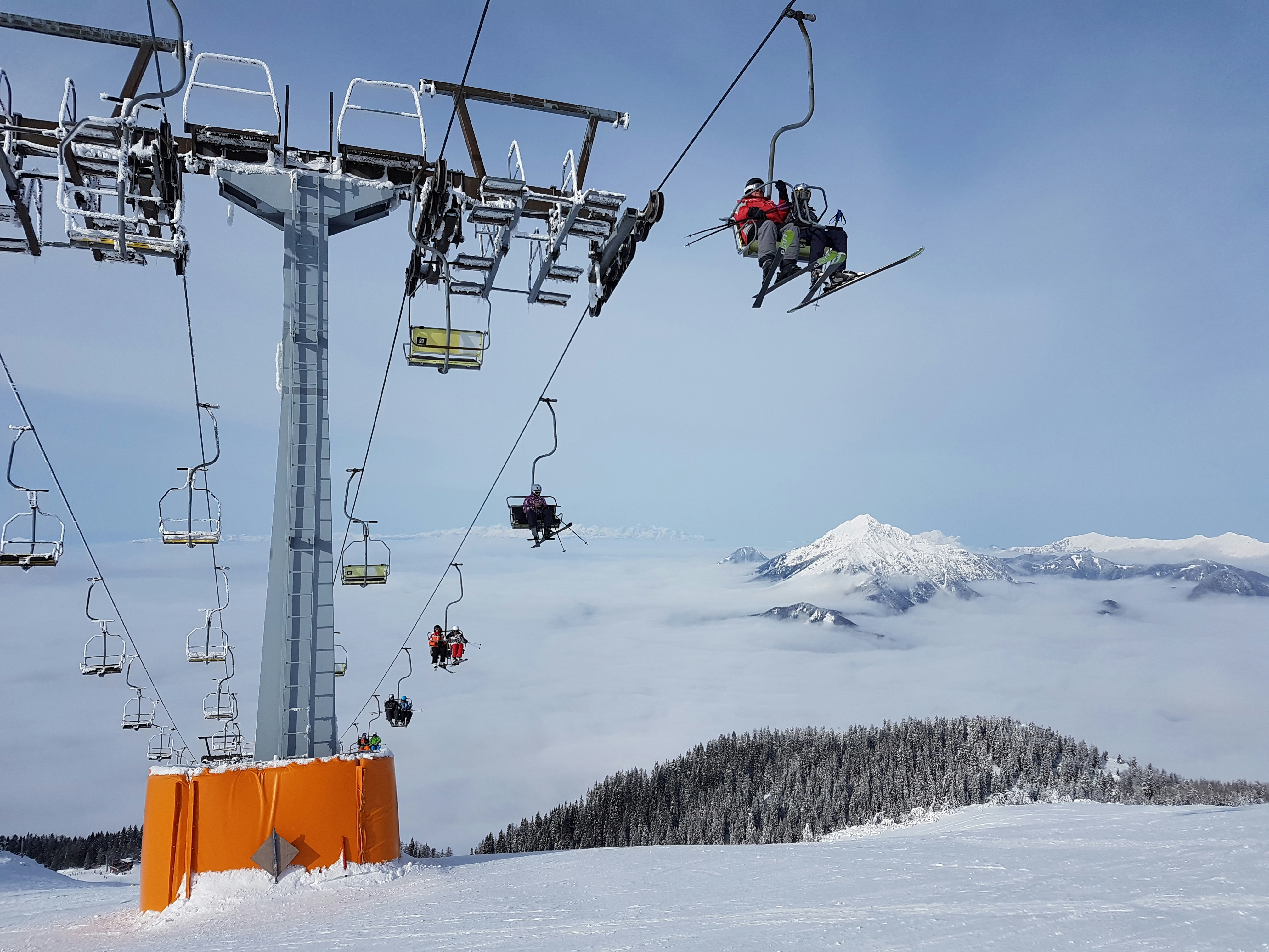 man in red jacket riding on cable car during daytime, skiers on a ski lift in a ski resort in Slovenia 