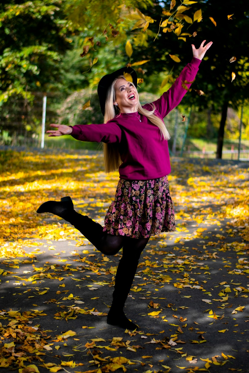 girl in pink jacket and black skirt standing on road with yellow leaves during daytime