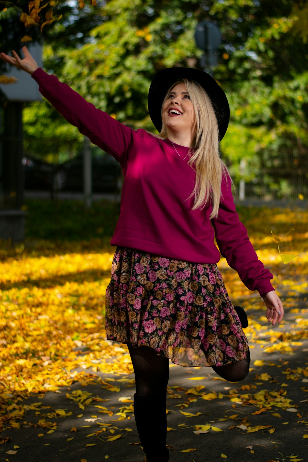 woman in pink long sleeve shirt and black and white floral skirt standing on yellow leaves
