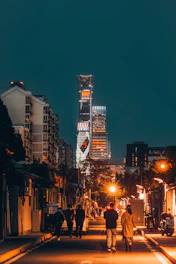Vibrant cityscape at dusk with glowing streetlights and shadowed figures walking.