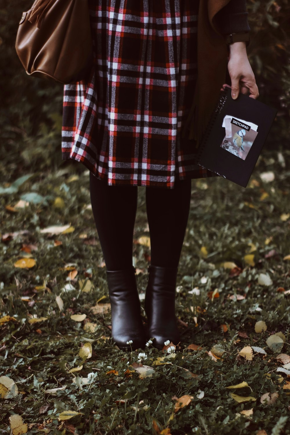 Person in schwarzen Lederstiefeln auf getrockneten Blättern stehend