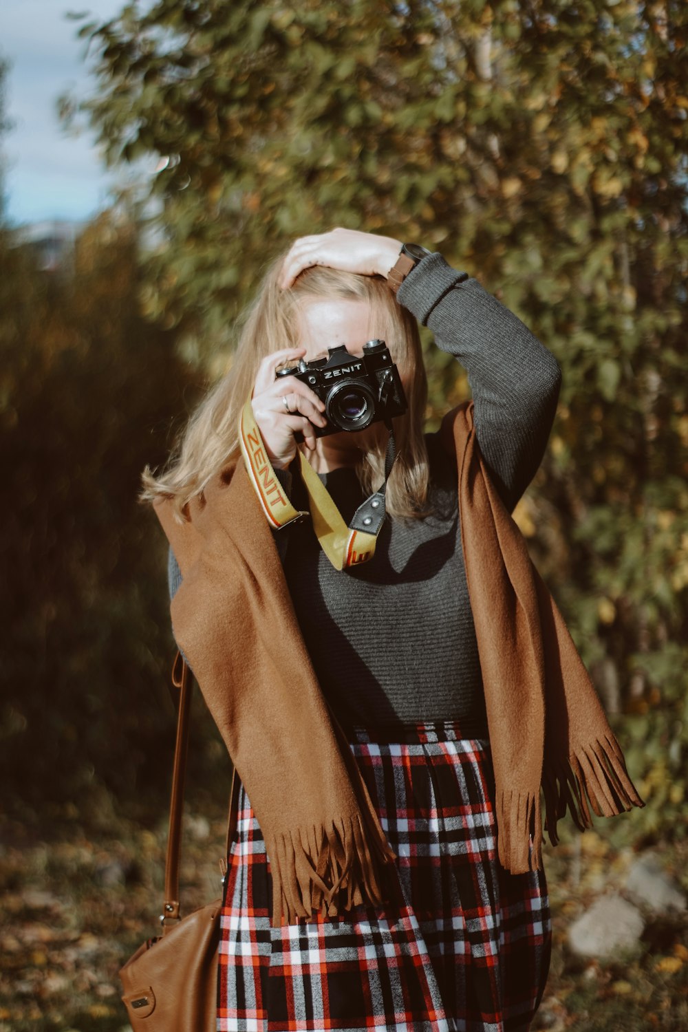 Femme en manteau marron tenant un appareil photo reflex numérique noir