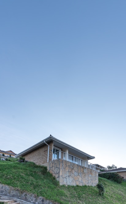 A sleek single-story home nestled in lush green hills overlooking the Atlantic Ocean under a clear blue sky.