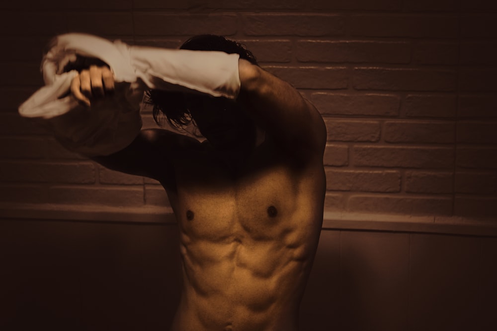 topless man standing near brown brick wall