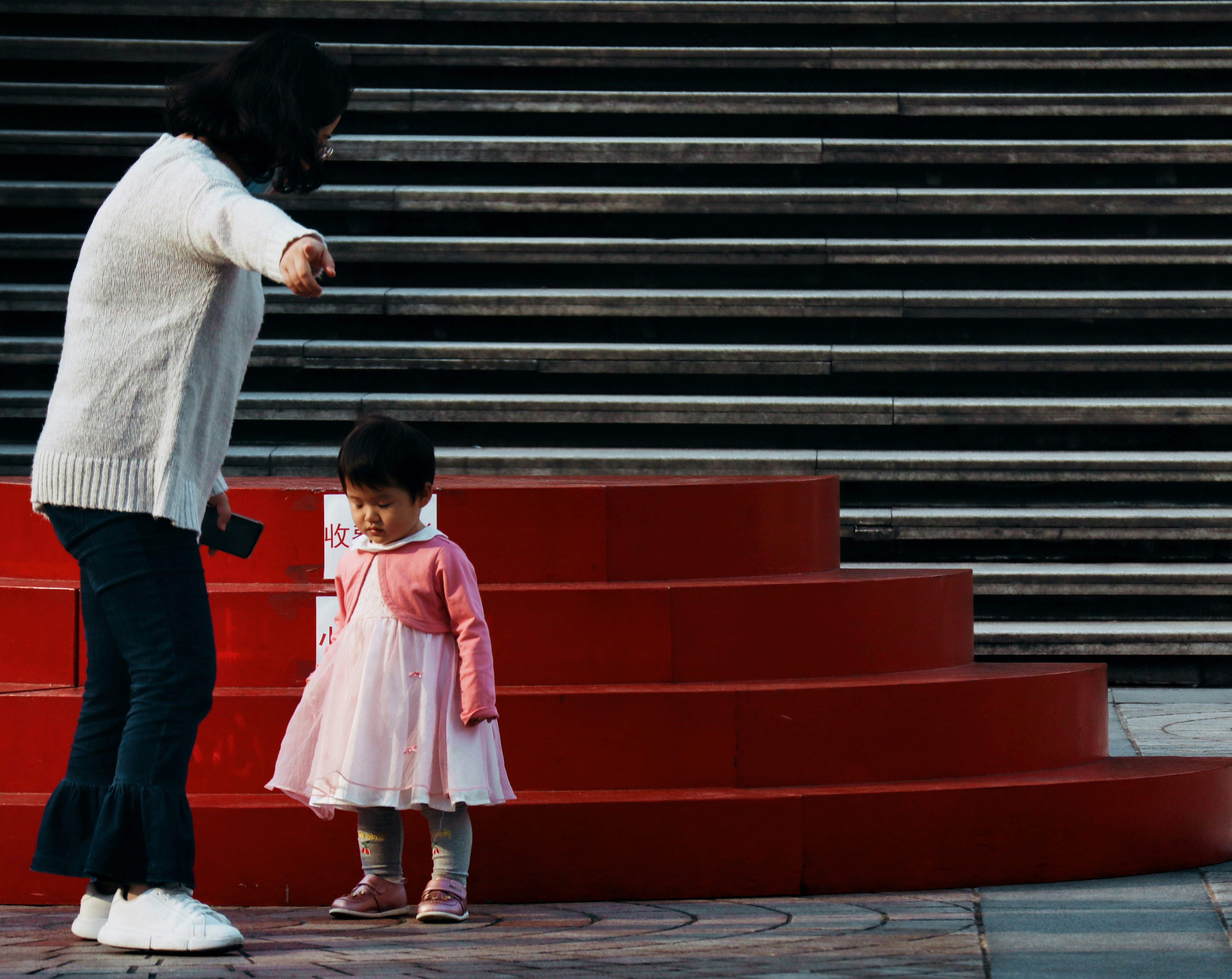 Gadis dengan kemeja lengan panjang putih dan celana merah berdiri di samping anak laki-laki dengan lengan panjang putih