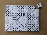 A collection of white dice arranged neatly on a brown surface, mostly displaying various numbers of black dots. Some dice have the word 'Bicycle' printed in red. One dice is slightly out of line on the top right.