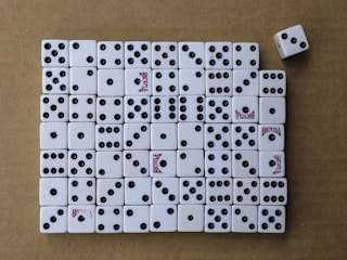 A collection of white dice arranged neatly on a brown surface, mostly displaying various numbers of black dots. Some dice have the word 'Bicycle' printed in red. One dice is slightly out of line on the top right.
