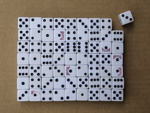 A collection of white dice arranged neatly on a brown surface, mostly displaying various numbers of black dots. Some dice have the word 'Bicycle' printed in red. One dice is slightly out of line on the top right.
