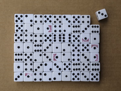 A collection of white dice arranged neatly on a brown surface, mostly displaying various numbers of black dots. Some dice have the word 'Bicycle' printed in red. One dice is slightly out of line on the top right.