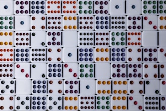 A collection of dominoes is arranged in a grid pattern, each displaying different combinations of colored dots. The dots come in various colors, including orange, purple, yellow, red, green, and blue. The domino pieces are set against a clean, white background.