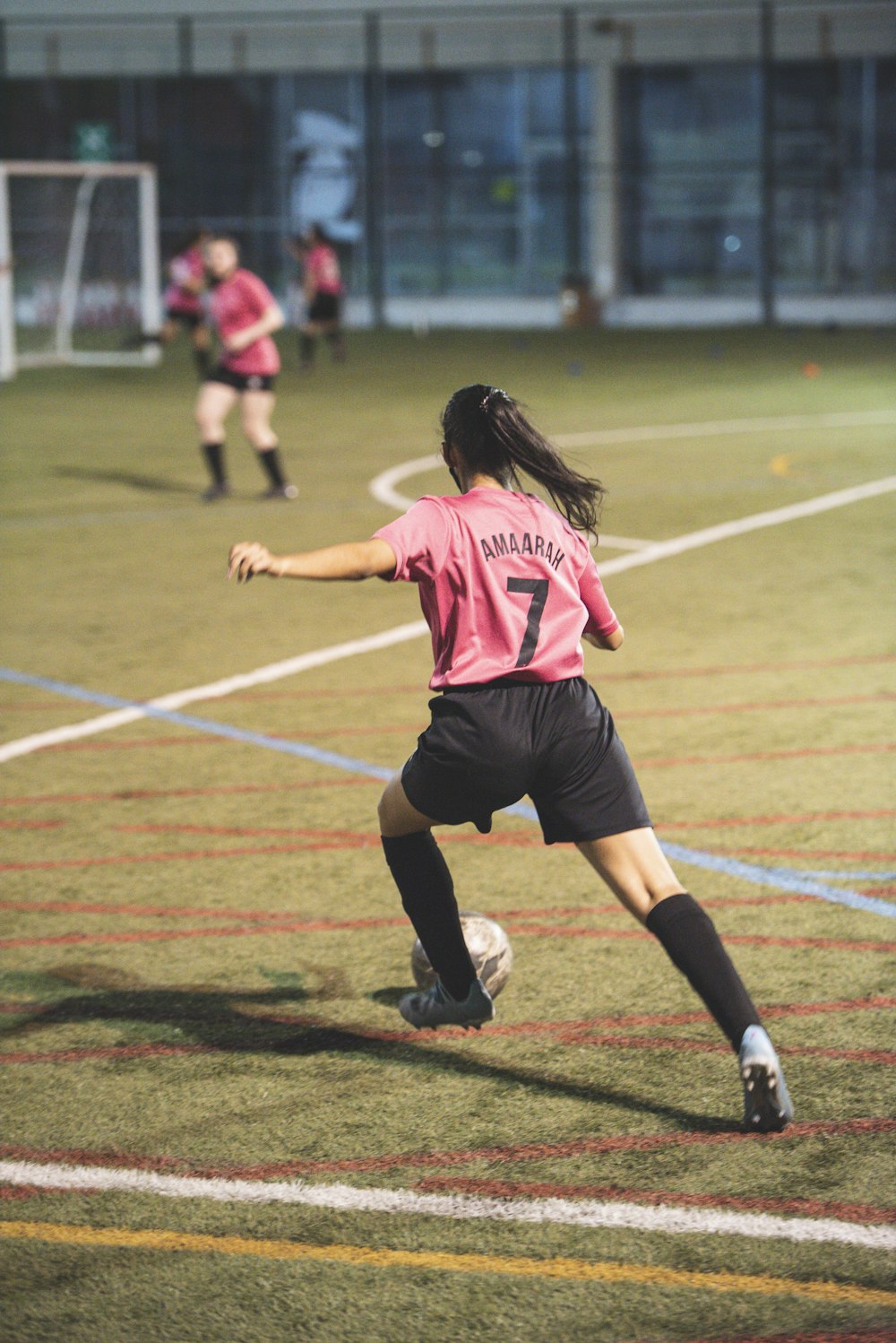 Donna in maglia da calcio rossa e bianca e pantaloncini neri che corre sul campo durante il giorno