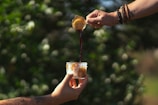 A barista pouring fresh espresso into a ceramic mug with a backdrop of forest greenery.
