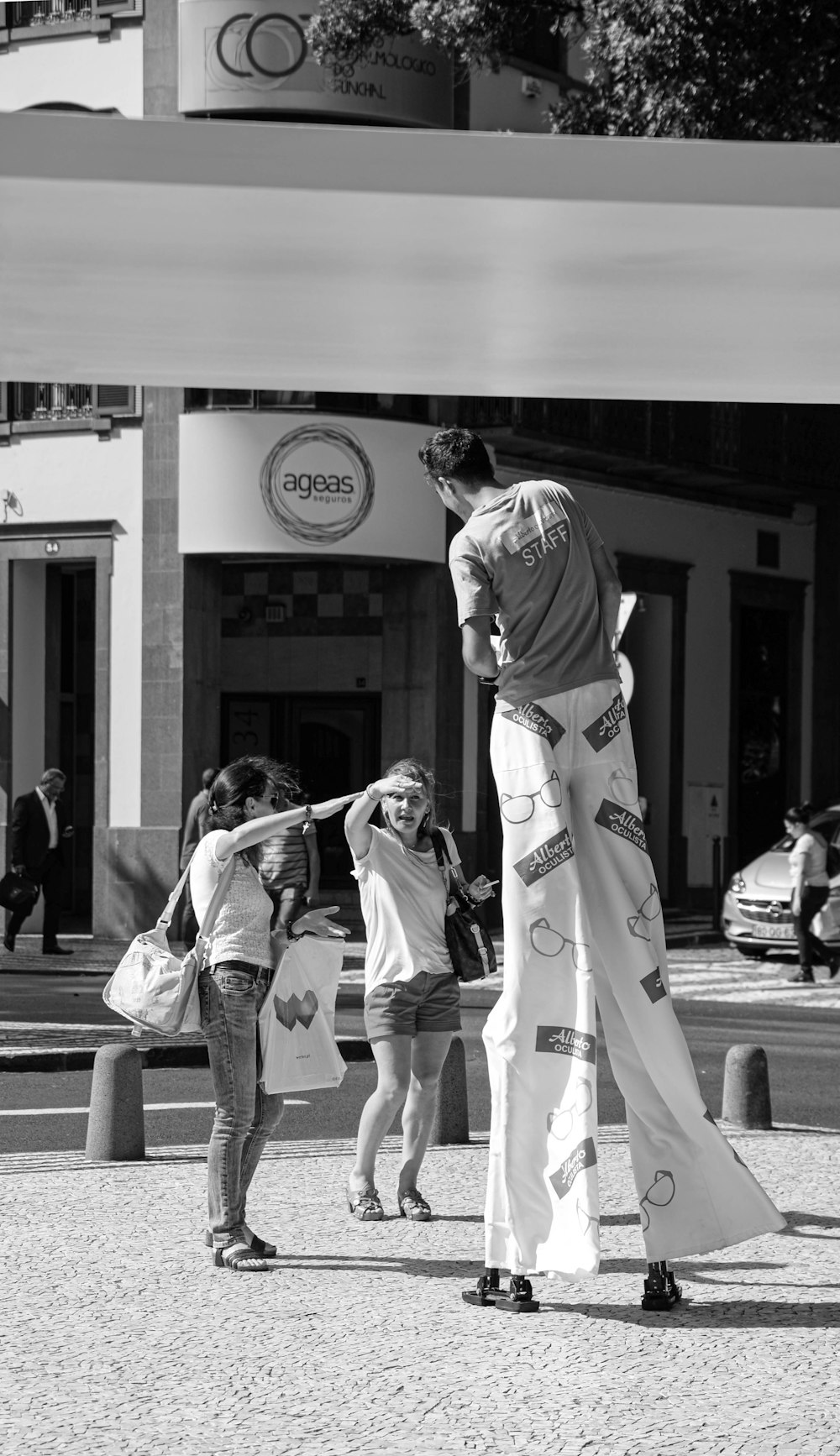 grayscale photo of man in white shirt and pants standing on sidewalk