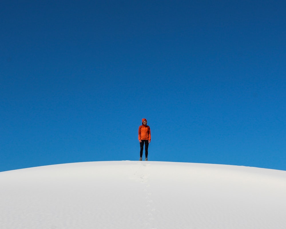 man in orange jacket standing on white sand during daytime
