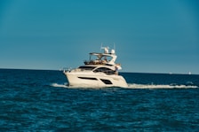 A luxury yacht is cruising through a calm, blue sea, with people on board enjoying the view. The sky is clear, and the ocean stretches into the horizon.