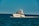 A luxury yacht is cruising through a calm, blue sea, with people on board enjoying the view. The sky is clear, and the ocean stretches into the horizon.