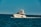 A luxury yacht is cruising through a calm, blue sea, with people on board enjoying the view. The sky is clear, and the ocean stretches into the horizon.