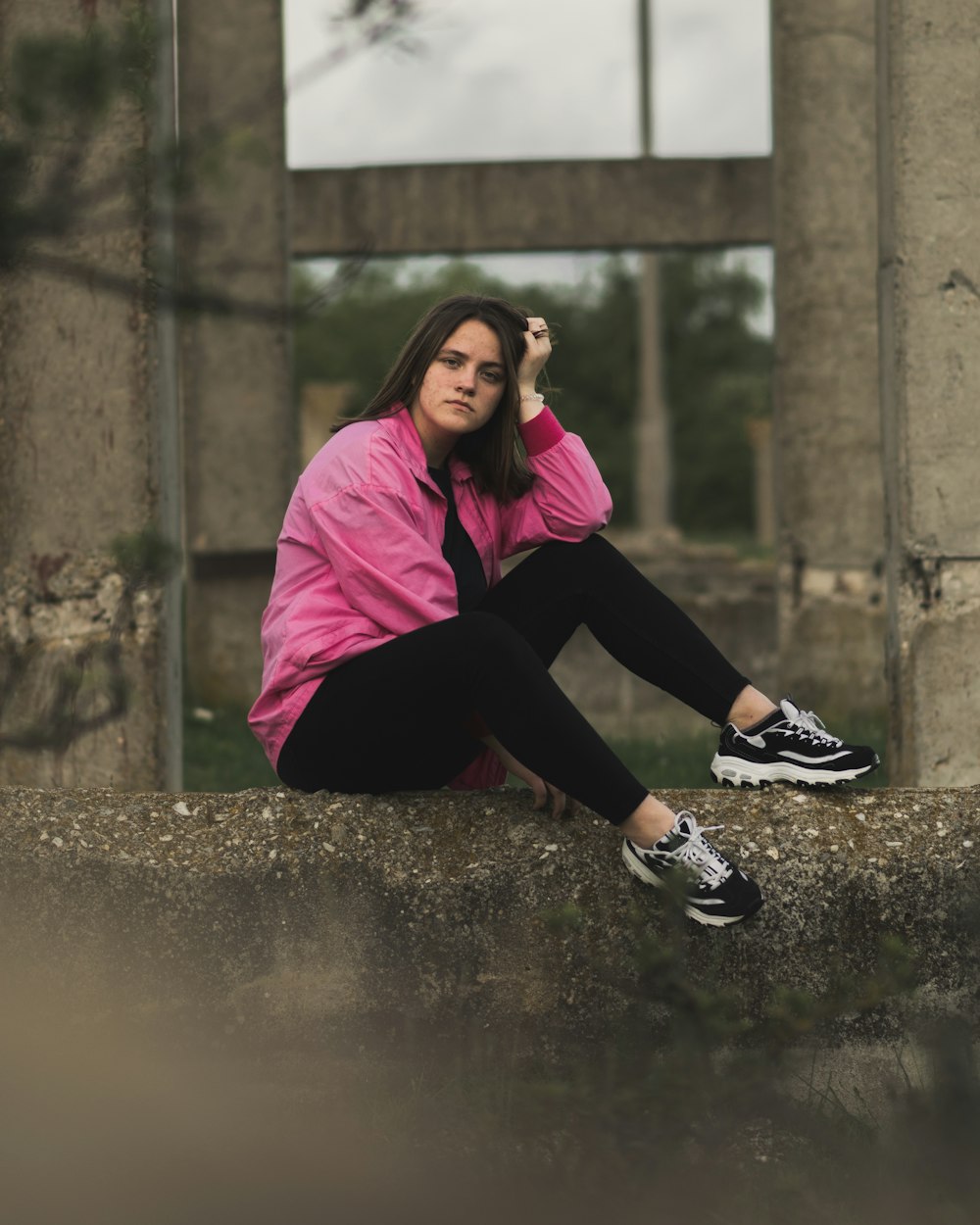 a woman in a pink jacket is sitting on a ledge