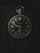 A vintage pocket watch with a black face and gold numbers and hands, showing signs of wear and scratches. It is placed against a dark fabric background, emphasizing its classic design and aged appearance. The watch features a smaller second dial at the bottom and a crown at the top for winding.