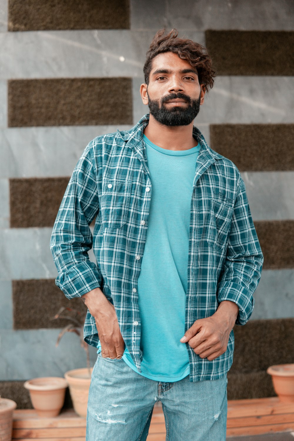 man in blue and white plaid dress shirt standing near brown brick wall