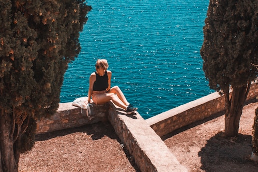 woman in black tank top sitting on concrete wall near body of water during daytime