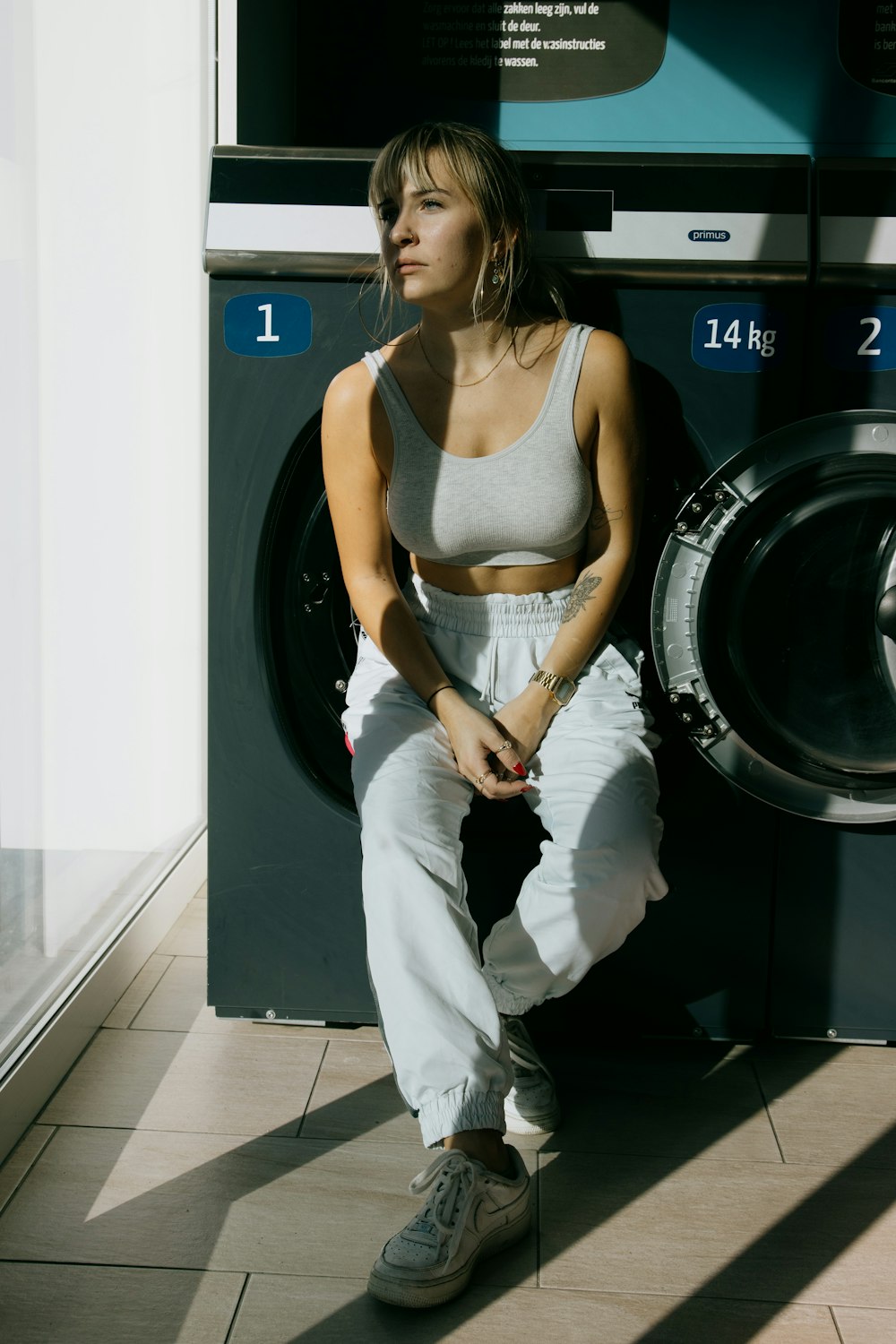 woman in white pants and white tank top standing beside front load washing machine