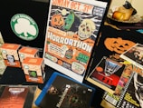 A collection of Halloween-themed memorabilia, including a poster advertising a horror movie marathon on October 31st, several boxes of Halloween masks with different designs, a CD case for a movie soundtrack, a Blu-ray cover for Halloween 3, and various thematic flyers and advertisements. The scene is set against a dark backdrop.