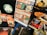 A collection of Halloween-themed memorabilia, including a poster advertising a horror movie marathon on October 31st, several boxes of Halloween masks with different designs, a CD case for a movie soundtrack, a Blu-ray cover for Halloween 3, and various thematic flyers and advertisements. The scene is set against a dark backdrop.