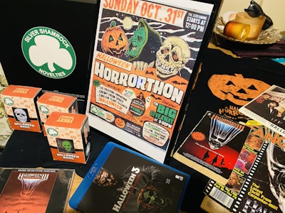 A collection of Halloween-themed memorabilia, including a poster advertising a horror movie marathon on October 31st, several boxes of Halloween masks with different designs, a CD case for a movie soundtrack, a Blu-ray cover for Halloween 3, and various thematic flyers and advertisements. The scene is set against a dark backdrop.