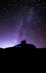 silhouette of person sitting on car under starry night