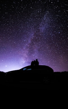 silhouette of person sitting on car under starry night