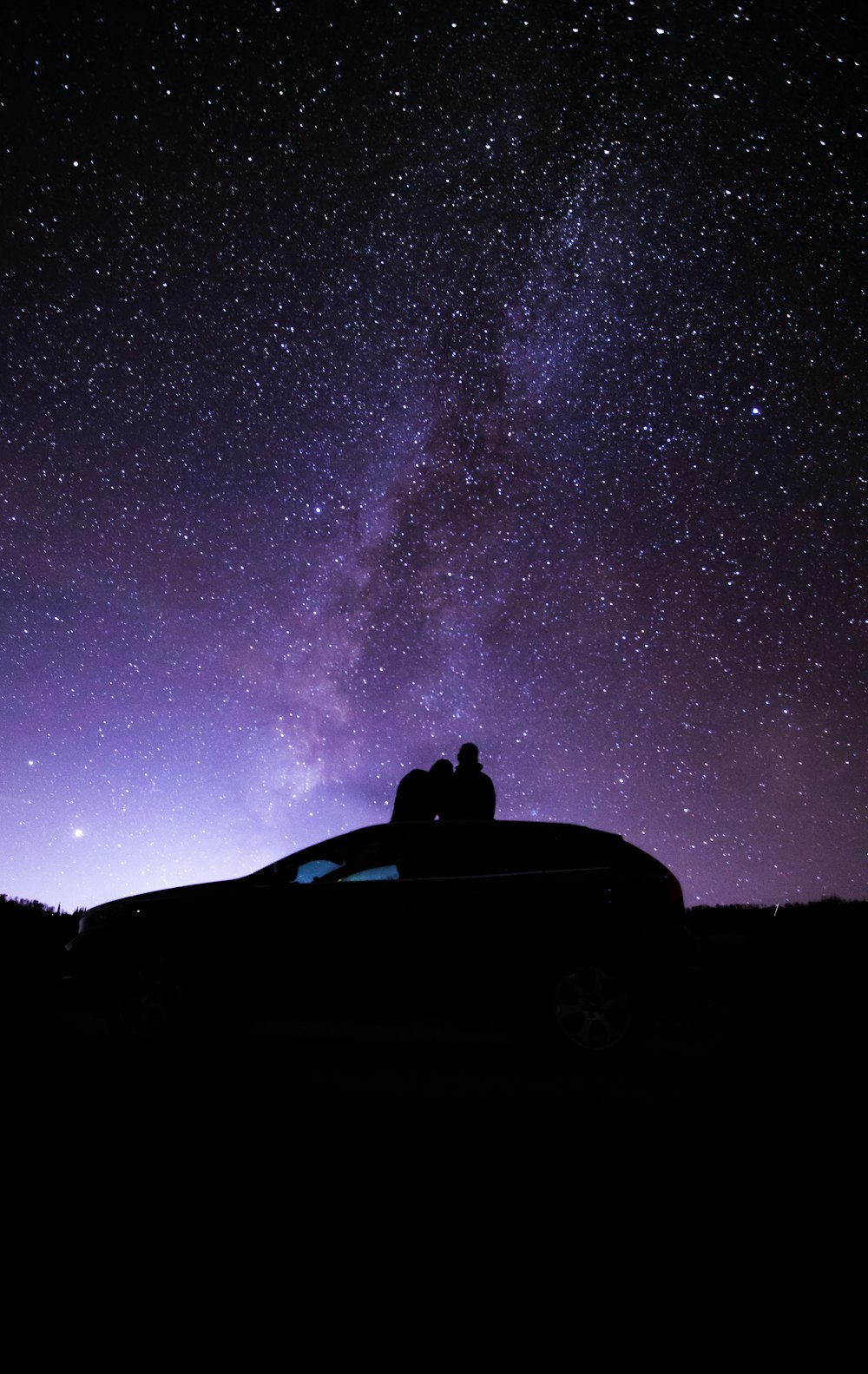 silhouette of person sitting on car under starry night