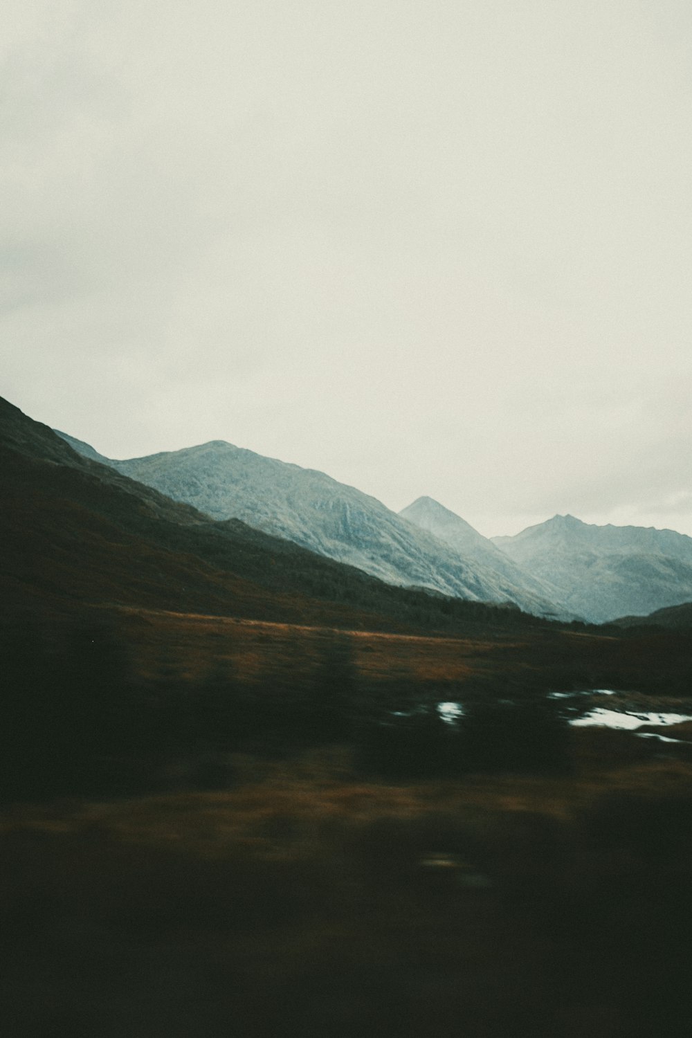 lake near mountains under white sky during daytime