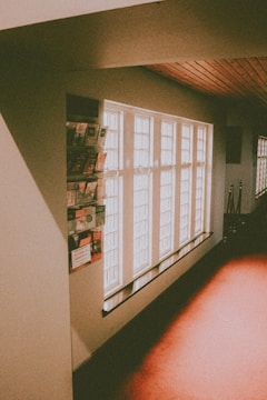 A hallway is illuminated with soft natural light streaming through several large, rectangular windows. The walls are adorned with various informational pamphlets and brochures. The flooring and ceiling feature a warm wooden tone, creating a cozy atmosphere.